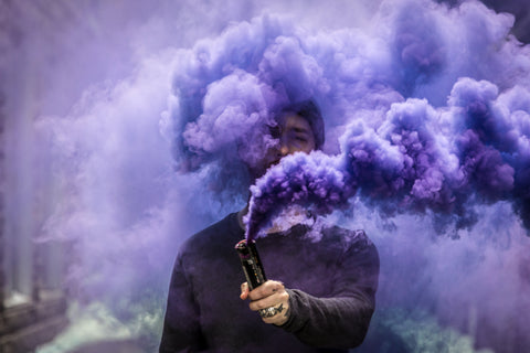 man with tattooed hand holding vaping device making purple clouds